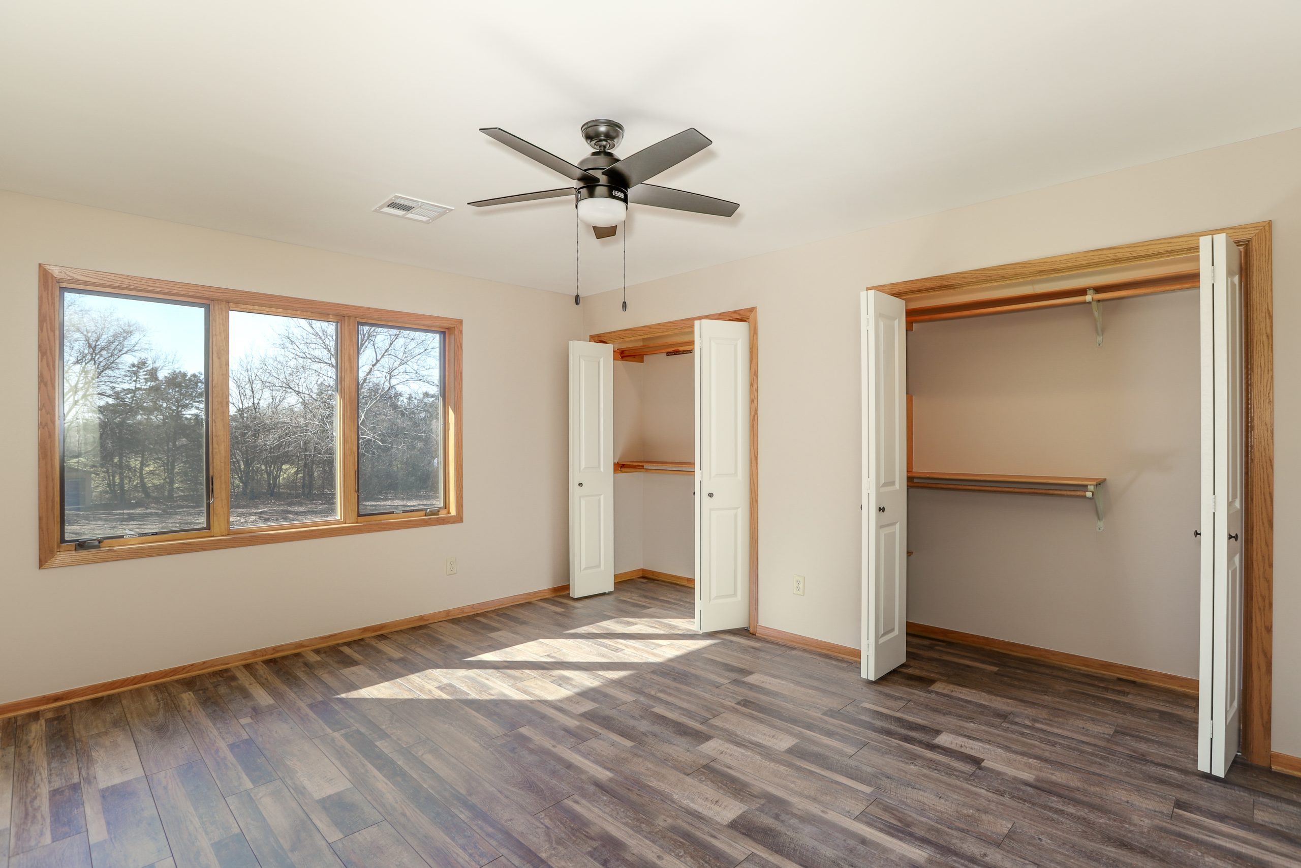Empty bedroom with large windows, wood trim, and open closets showing hanging rods and shelves.