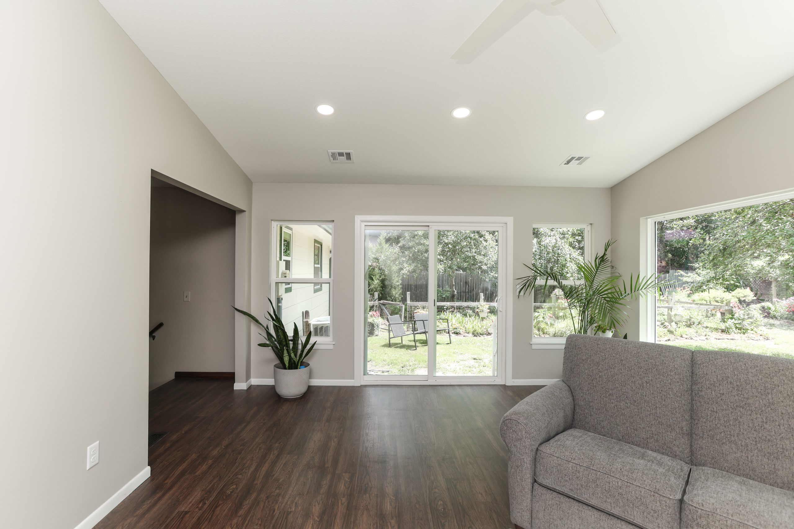 Bright living room with large windows overlooking a garden, gray walls, and dark wood flooring beside a gray sofa.