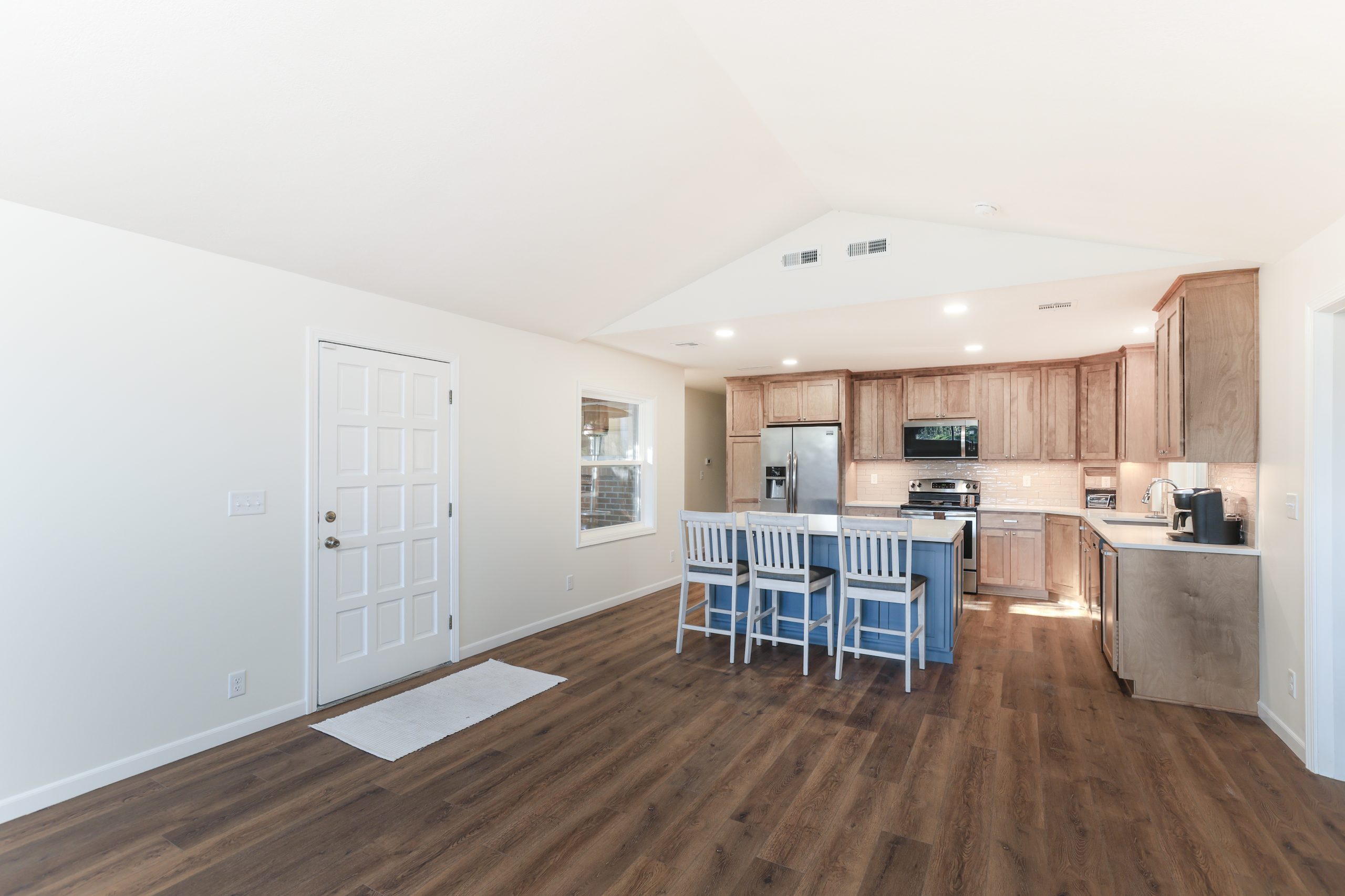 Bright open kitchen with wooden cabinets, stainless appliances, and a blue island/bar counter with white stools