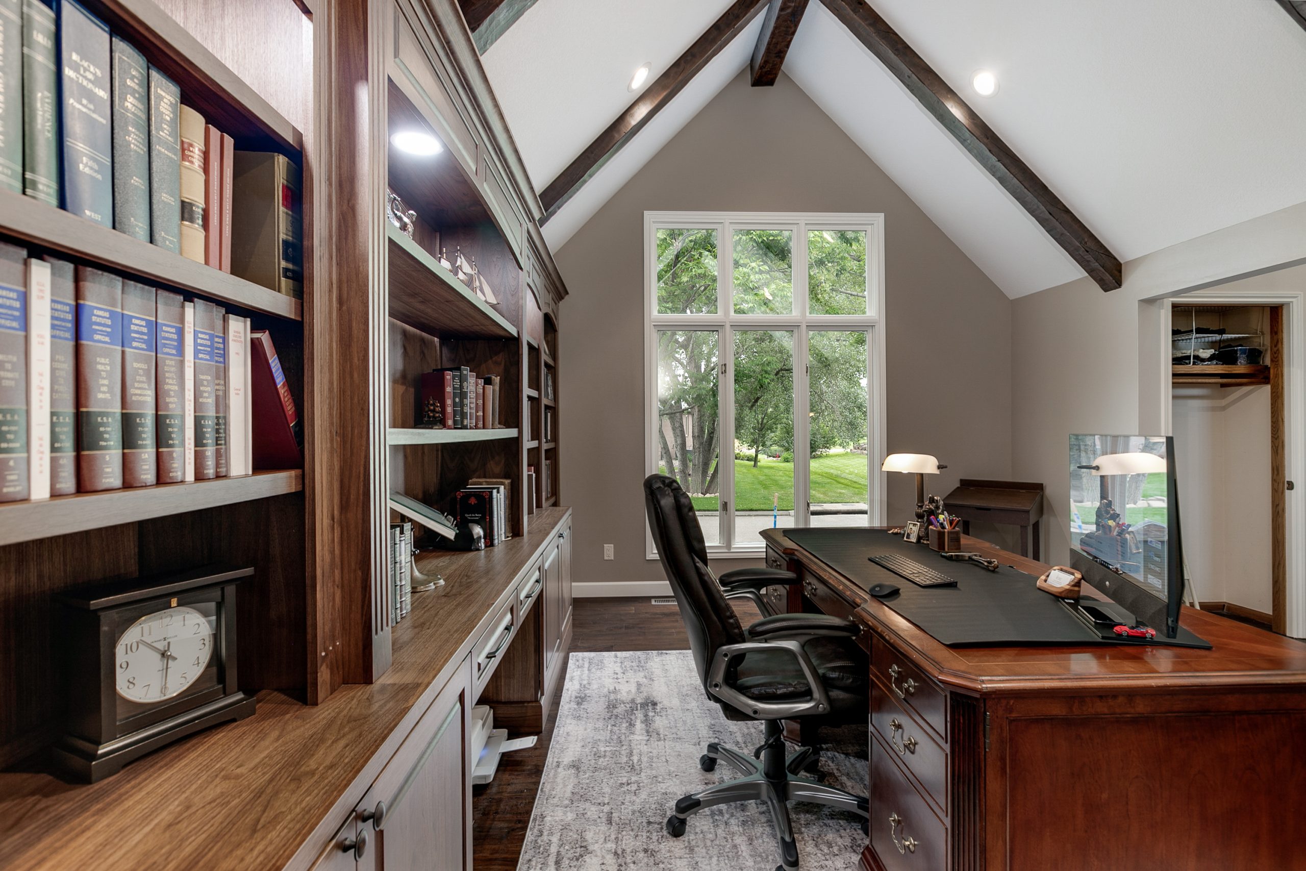 Home office with dark wood built-in shelves filled with books, a large wooden desk, and a window with trees outside